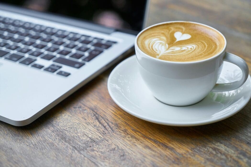 Cana de cafea / cappuccino langa laptop pe birou